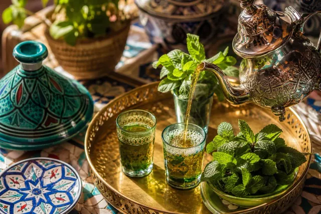 Moroccan mint tea poured from a silver teapot into a decorated glass with fresh mint