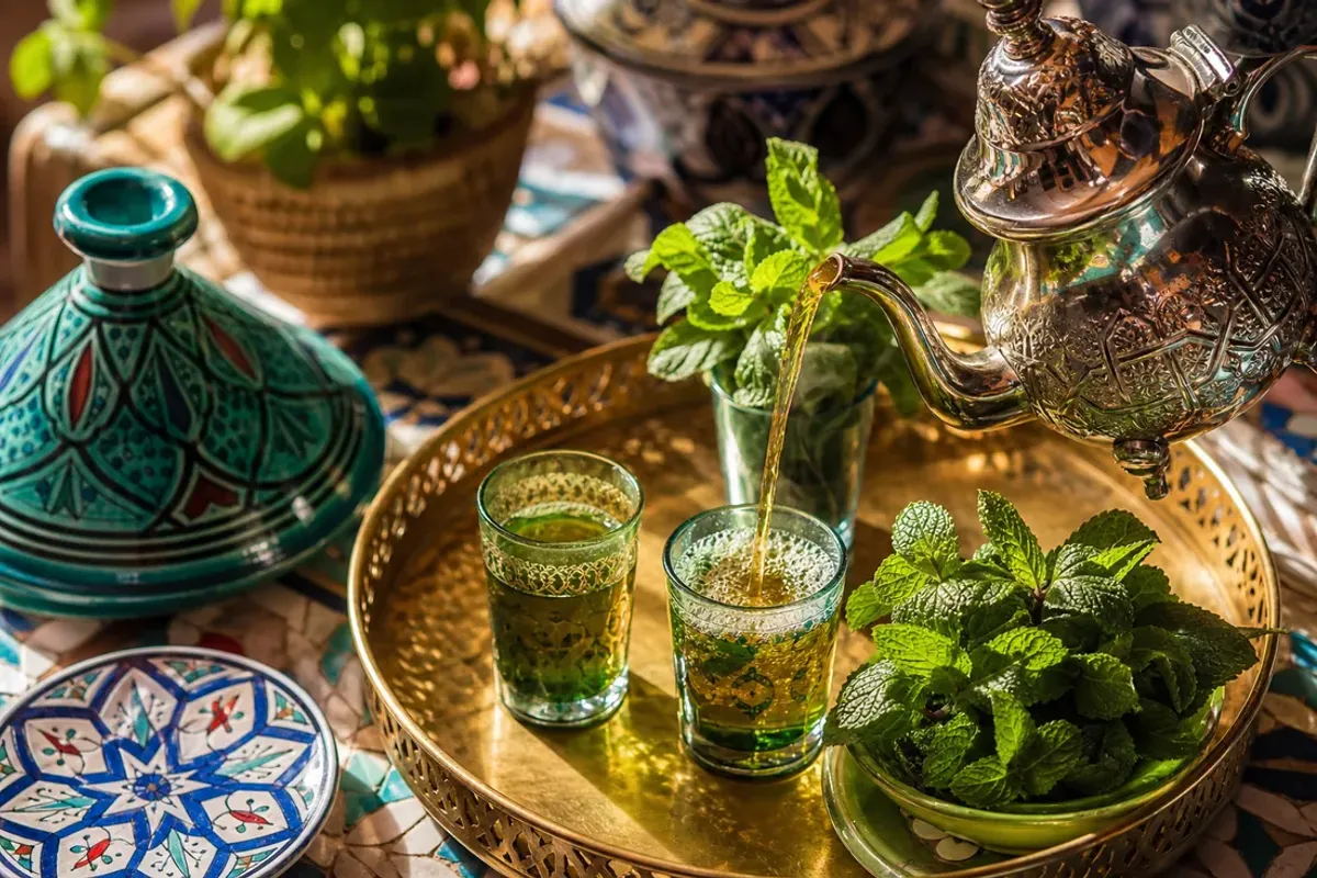Moroccan mint tea poured from a silver teapot into a decorated glass with fresh mint